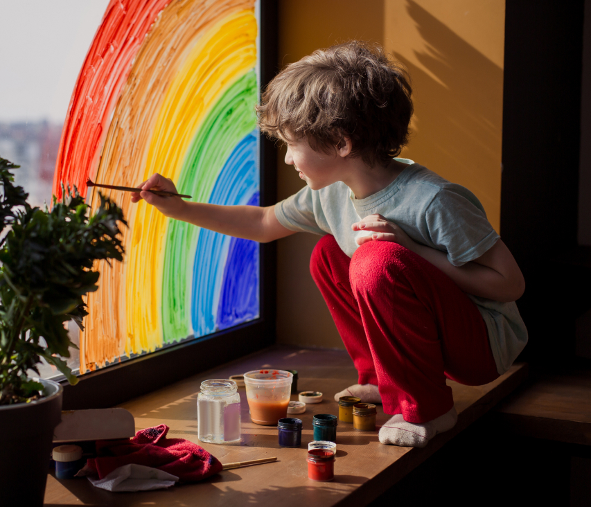 Young boy painting a rainbow on a window