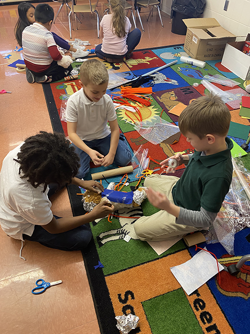 Kids seated on the floor interacting with each other and building something together with tape, foil and scissors