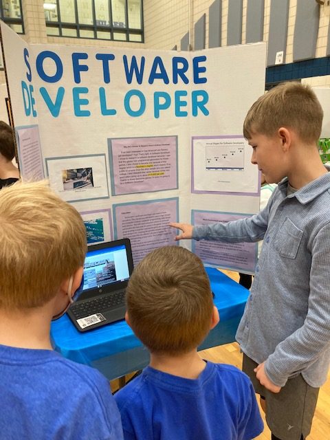 Young child presenting to two other children his project board on being a Software Developer