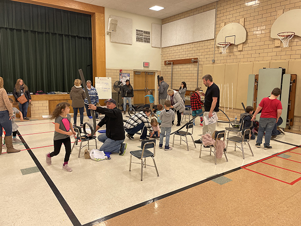 Kids in a gymnasium building a racetrack with adults